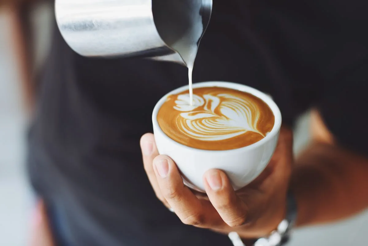Barista sirviendo leche vaporizada para formar latte art en un cappuccino