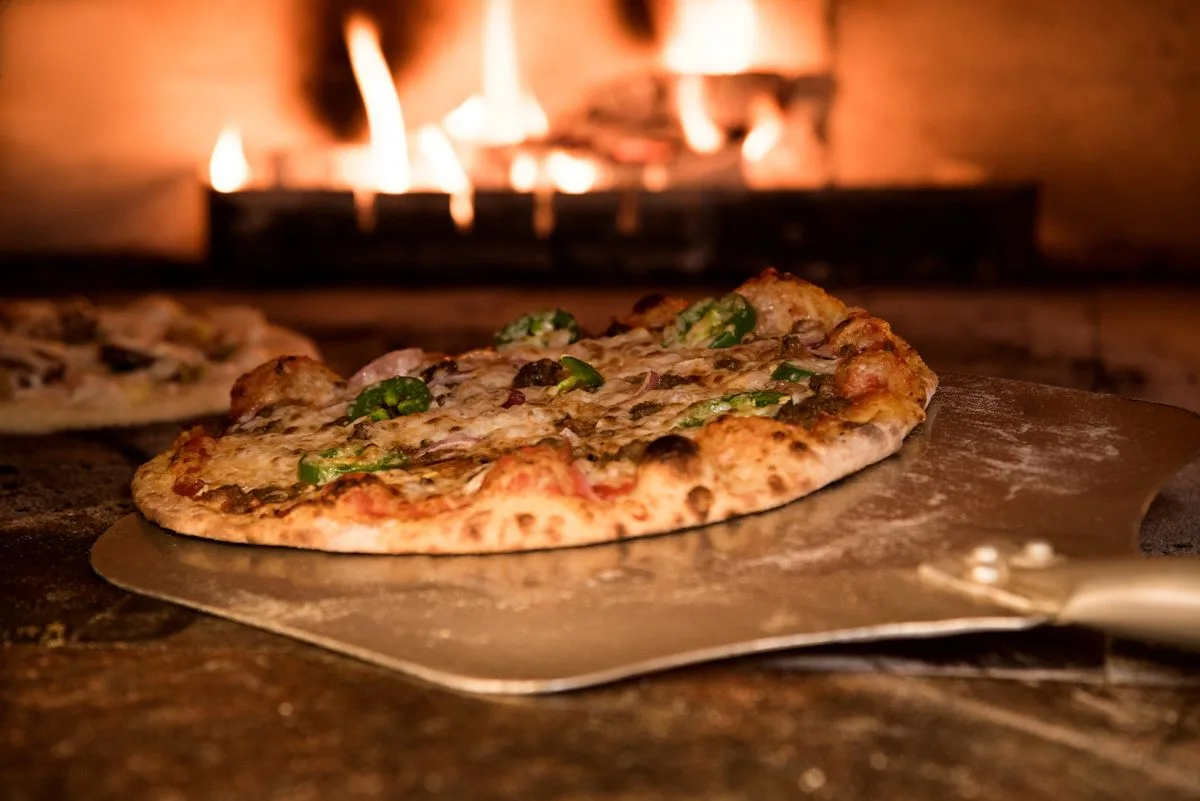 Pizza sobre pala metálica entrando a un horno de leña encendido